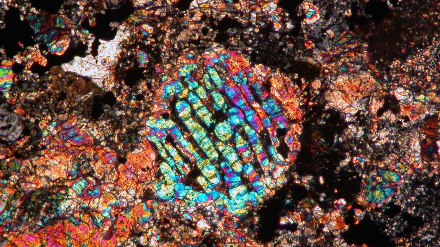 Colorful micrograph of a chondrule from the Chelyabinsk meteorite with iridescent patterns on a dark, grainy background.
                                 (AI-generated alt-text, generated with GPT-4.1-mini)