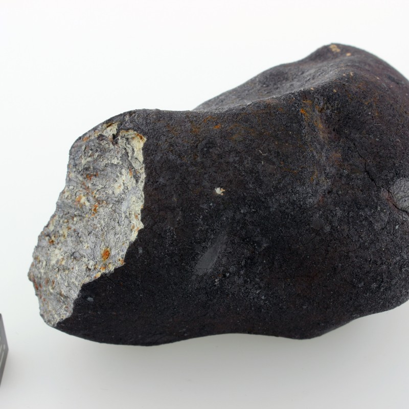 Dark, irregularly shaped meteorite with light fracture surface, cube with scale and letters beside it. (AI-generated
                                 alt-text, generated with GPT-4.1-mini)